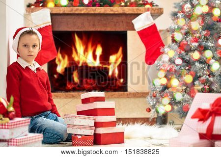 Happy boy near fireplace stacking gifts for Christmas .