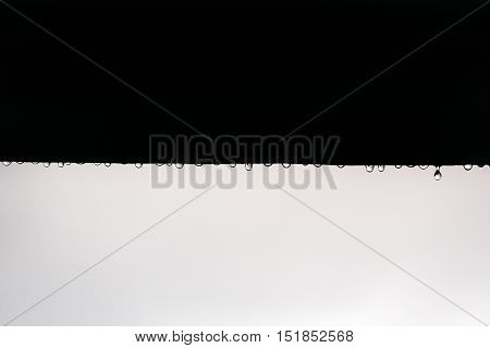 Small water drops of rain drip from roof black and white on grey sky background