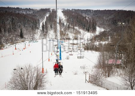 Mother and son rise on cableway on winter day at ski resort.