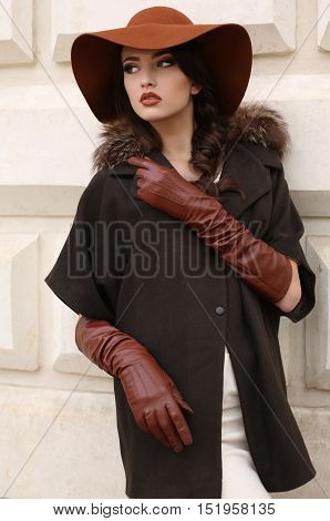fashion outdoor photo of gorgeous woman with dark hair in elegant luxurious coat wool hat and leather gloves walking by autumn city
