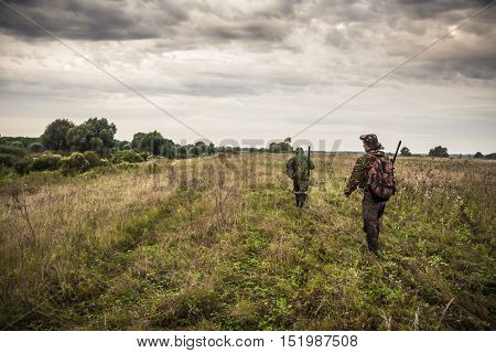Hunters going through rural field with dramatic sky during hunting season