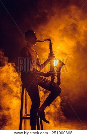 Young Expressive Jazzman Sitting On Stool And Playing Saxophone