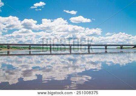 Steel Bridge With Lots Of Clouds In The Sky And Their Reflection In Water