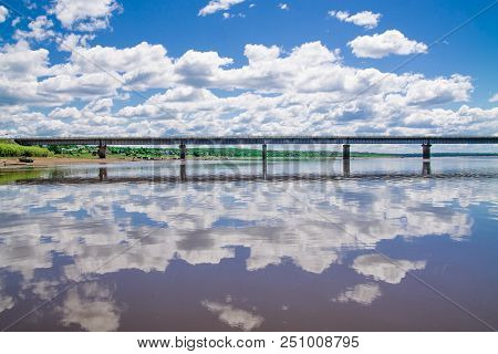 Steel Bridge With Lots Of Clouds In The Sky And Their Reflection In Water
