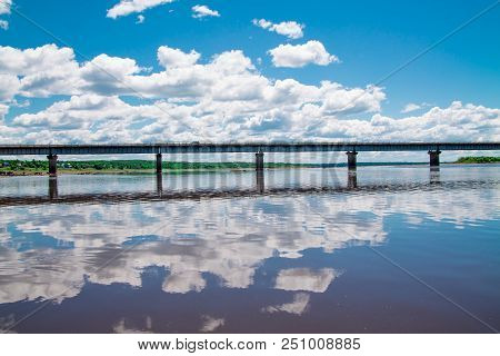 Steel Bridge With Lots Of Clouds In The Sky And Their Reflection In Water