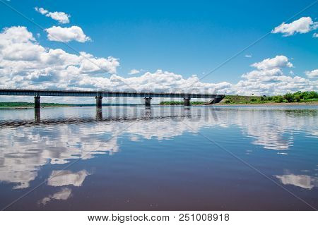 Steel Bridge With Lots Of Clouds In The Sky And Their Reflection In Water