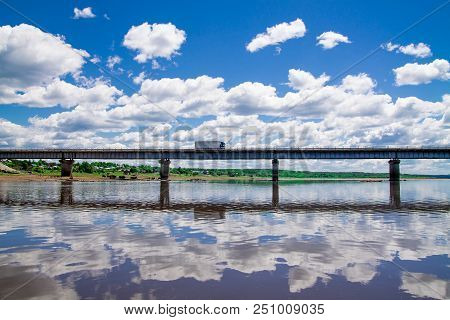 Steel Bridge With Lots Of Clouds In The Sky And Their Reflection In Water