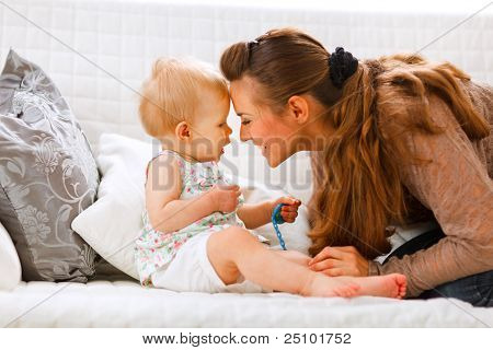 Cute Baby mit Schnuller und junge Mutter spielen auf Couch