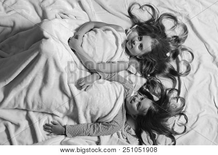 Girls Lie On White And Pink Bed Sheets Background. Kids With Happy Faces And Hearts In Hair Lie In B