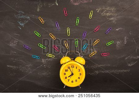 Yellow Alarm Clock And Clips On Black Chalkboard Top View. Concept: Back To School, School Holidays,