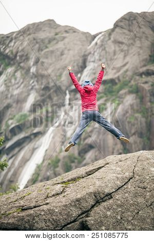 Happy Woman Jumping On Rock In Grey Mountains, Enjoying Traveling And Adventure.