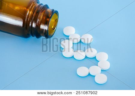 White Pills Spilling From A Medicine Bottle Forming A Dollar Sign On A Blue Background.