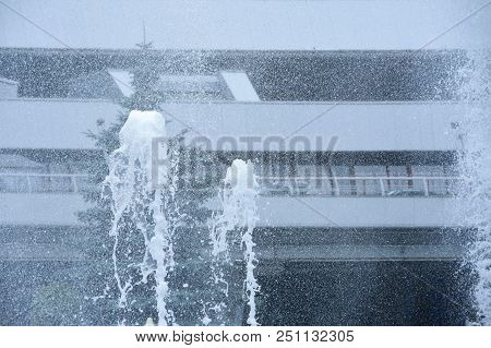 Splashes From The Fountain Fly Against The Background Of Modern Building Made Of Metal In Hot Weathe