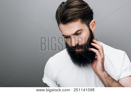 Horizontal Portrait Of Brutal Handsome Young Bearded Male Corrects His Moustache And Beard, Looking 