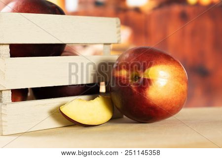 Lot Of Whole One Slice Of Ripe Deep Red Nectarine In A Wooden Crate With Rustic Kitchen In Backgroun