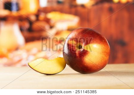 Group Of One Whole One Slice Of Ripe Deep Red Nectarine With Rustic Kitchen In Background