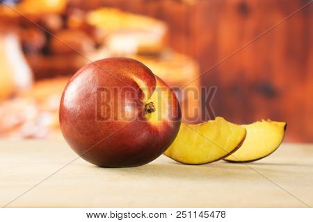Group Of One Whole Two Slices Of Ripe Deep Red Nectarine With Rustic Kitchen In Background