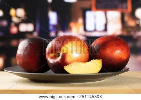 Group Of Three Whole One Slice Of Ripe Deep Red Nectarine On A Grey Ceramic Plate With Restaurant In