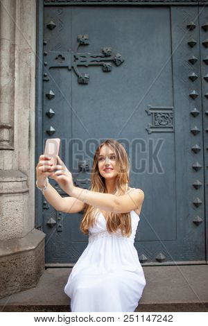 Jolly Girl In Dress Taking Selfie Against Old Metal Door. Smiling Attractive Young Woman Posing For 