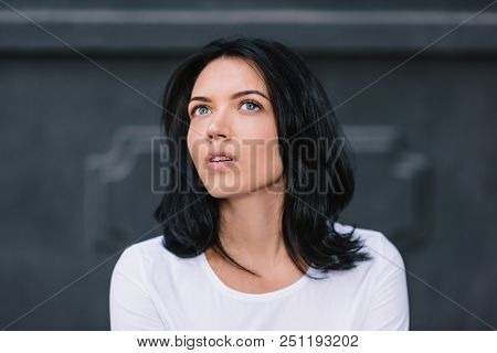 Portrait Of Doubtful Young Woman Wearing White T-shirt, Looking Sideways With Indecisive And Perplex