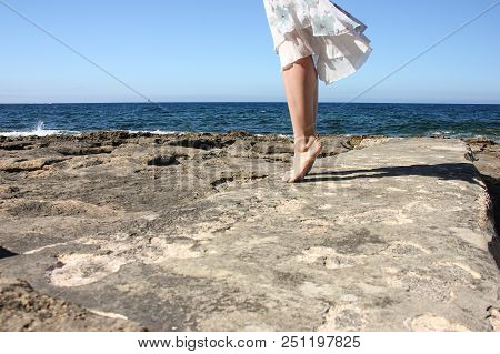 Legs Of Young Girl In White Fluttering Skirt Stand Tiptoe On Stone Beach