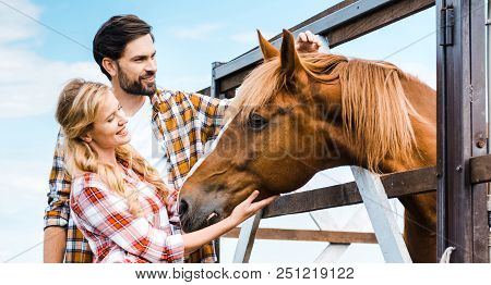 Couple Of Smiling Ranchers Palming Horse In Stable