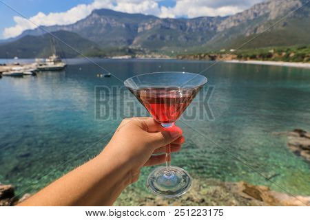 A Glass Of Red Martini In The Woman Hand On The Background Of A Picturesque Seascape, Summer Vacatio