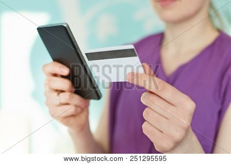 Cropped Image Of Modern Smart Phone And Plastic Card In Woman`s Hands Against Blue Blurred Backgroun