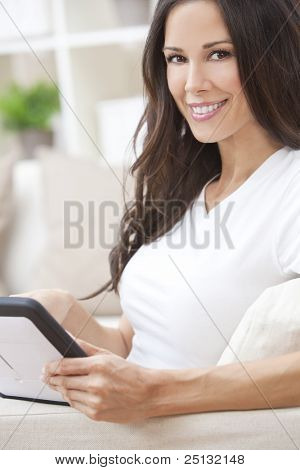 Giovane e bella donna bruna a casa seduto sul divano o divano utilizzando il suo tablet PC o ipad un