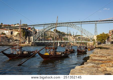 View Of The Douro River With Rabelo Boats, The Iconic Dom Luis Bridge And The Ribeira Neighbourhood 