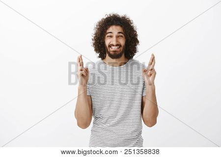 Indoor Shot Of Anxious Believing Eastern Bearded Man With Afro Hairstyle, Raising Crossed Fingers An