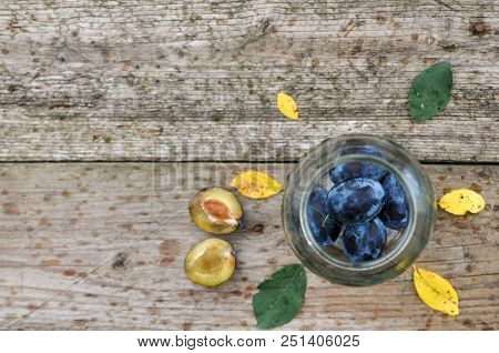 Harvest Purple Plums For Canning In A Glass Jar On A Wooden Background, Yellow And Green Leaves. Rus