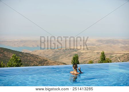 Young Woman Relaxaing In The Swimming Pool Looking At The Nature Landscape View On Background. Trave