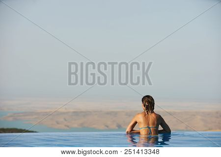 Young Woman Relaxaing In The Swimming Pool Looking At The Nature Landscape View On Background. Trave