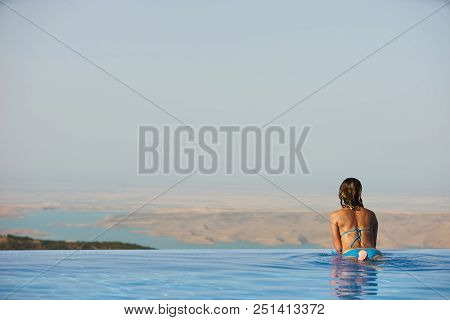 Young Woman Relaxaing In The Swimming Pool Looking At The Nature Landscape View On Background. Trave