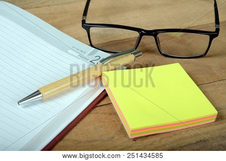 A Wooden Ball-pen, Open Diary And Note-pad With Eye-glasses On Wooden Background