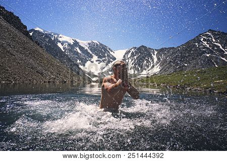Young Man Swimming In A Mountain Lake On Background Of Beautiful Mountain Landscape With Snow-capped