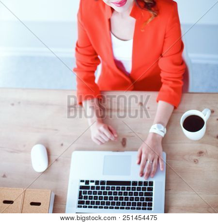 Attractive woman sitting at desk in office, working with laptop computer
