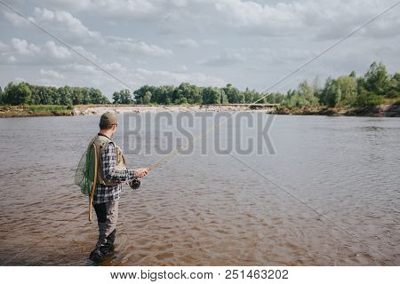 A Picture Of Man Standing In Water And Fishing. He Is Holding Spinning In Hands And Looking At Water