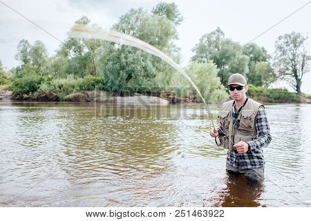 A Picture Of Man Holding Fly Rod. It Is Vibrating. Guy Holds Part Of Spoon In The Other Hand. He Sta