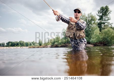 Fisherman In Action. Guy Is Throwing Spoon Of Fly Rod In Water And Holding Part Of It In Hand. He Lo