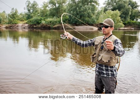 Serious Fisherman Stands On Shallow An Waving With Fly-fishing. Also He Has A Spoon In Other Hand. G