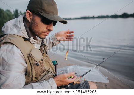 Serious Man With Sunglasses Is Sitting At The Edge Of Water And Looking Down. He Is Holding Spoon Wi