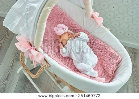 Cute Newborn Baby Girl With Hand In Mouth. Lullaby Moses Basket.