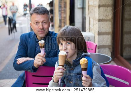 Father and son eating ice-cream in street cafe, family lifestyle. Dad with ofspring enjoying icecream spring outdoor