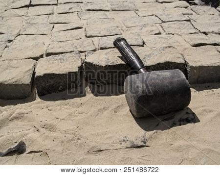 An Old Shabby Huge Mallet Lies At The Workplace Of The Unfinished Paving Stones. Beautiful Building 