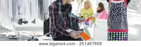 Portrait Of A Clothing Designer Sitting On A Desk In The Studio.