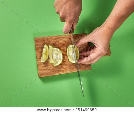 Top view of girl cutting a half of organic ripe lime with slices on a brown board on a green background. A sharp knife in her hands.