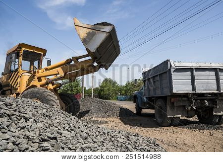 Yellow Loader Delivering Stone Gravel Into Truck During Road Construction Works. The Stones For The 