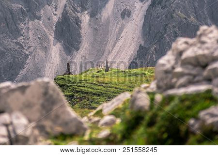 Tourists In Dolomites Valley, Italy. Standing On A Green Grass. Sourrounded By Mountains.